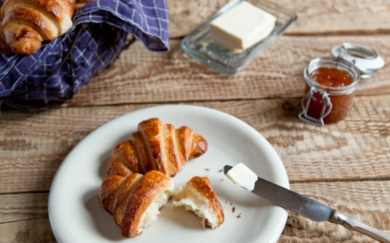 Čerstvý domácí croissant s máslem a džemem na bílém talíři
