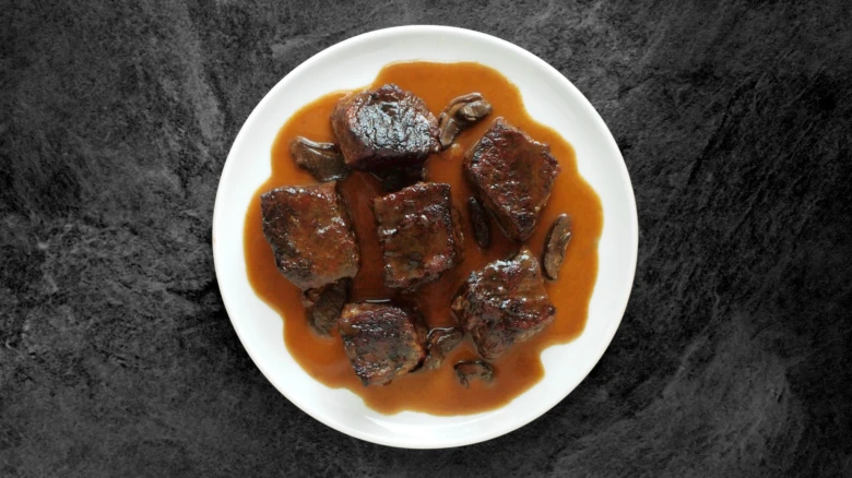 Příprava hovězího krku s houbovou omáčkou na bílém talíři.