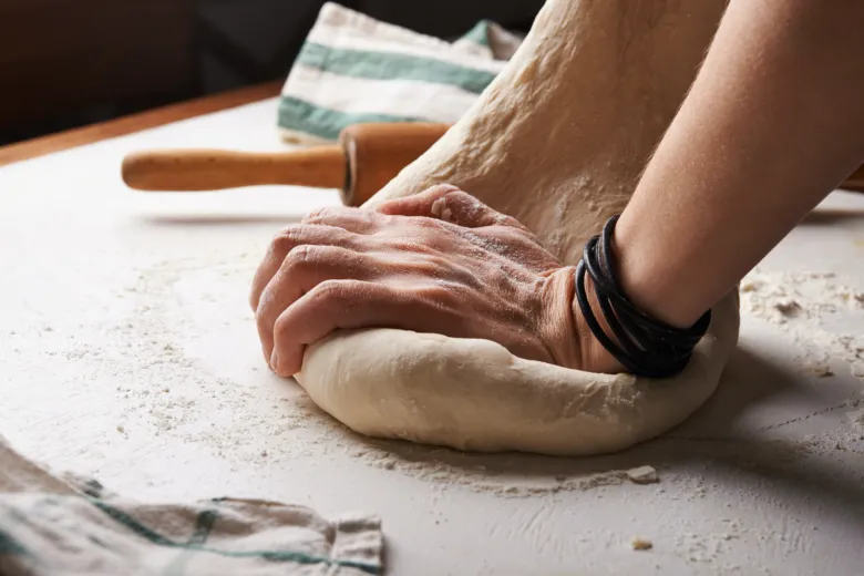 Ruce kynoucí nekynuté těsto na pizzu s moukou