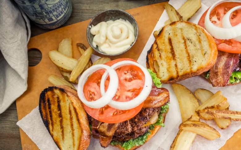 Domácí hovězí burgery s bramborami a omáčkou na dřevěném prknu.