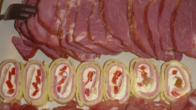 Sýrové rolády s uzeným masem a paprikou na talíři.