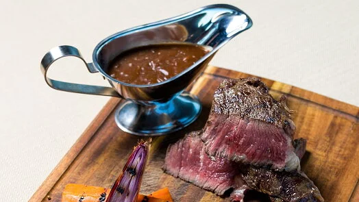 Smažený steak s omáčkou na dřevěném talíři.