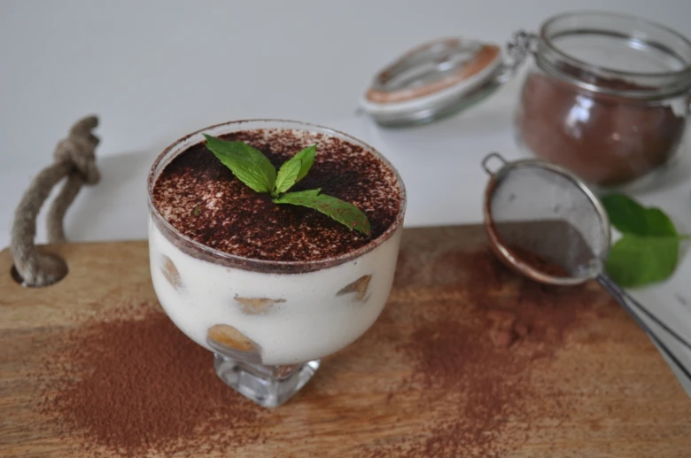 Hotový dezert Tiramisu s čokoládou a mátou na dřevěném podkladu.