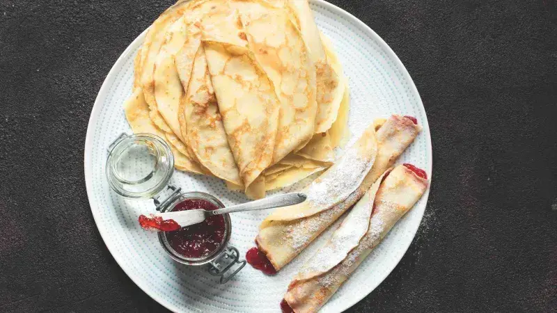 Palačinky s ovocnou marmeládou posypané cukrem na talíři.