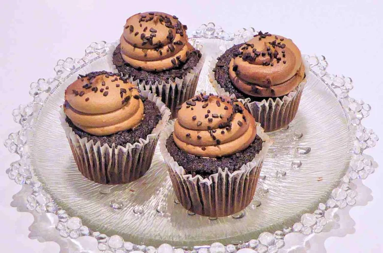 Čtyři čokoládové muffiny s krémem na skleněném podstavci.