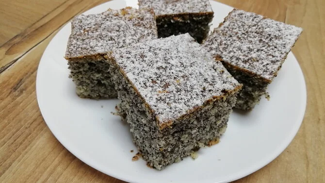 Kusy makového koláče posypané moučkovým cukrem na bílém talíři.