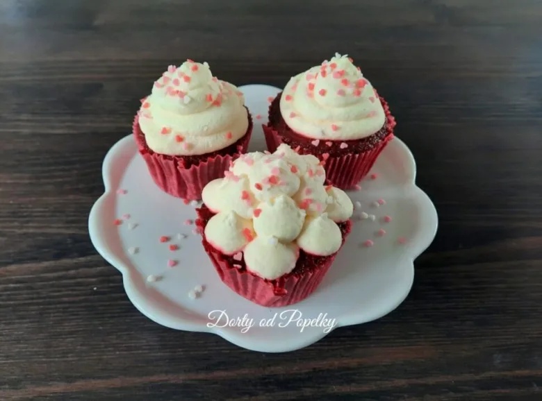 Tři červené muffiny s bílým krémem z mascarpone na talířku.