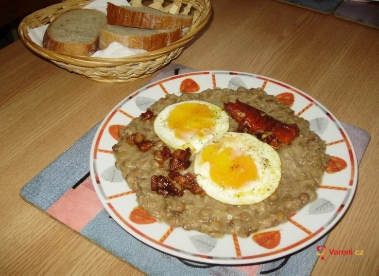 Čočka na kyselo s vejci a slaninou podávaná v talíři.