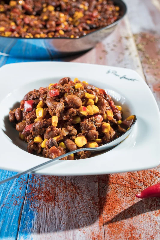 Bílá miska s chilli con carne na dřevěném stole.