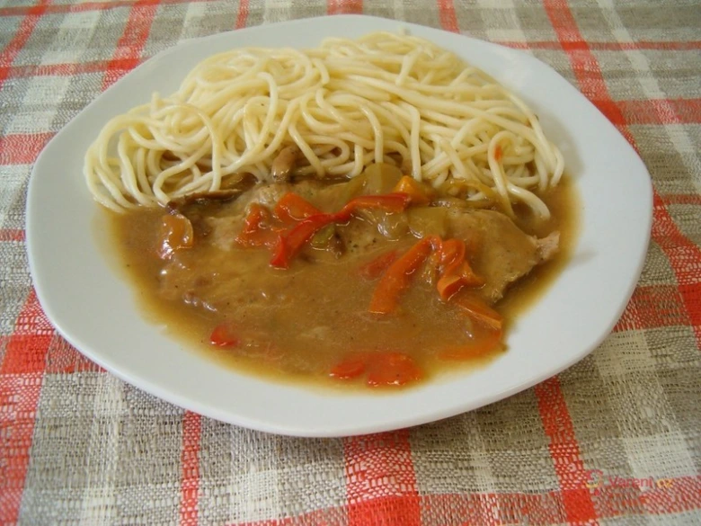 Pohár s špagetami a vepřovým masem ve tmavé omáčce.