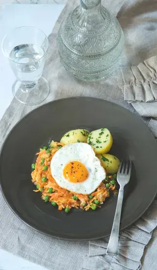 Dušená mrkev s hráškem podaný na talíři se smaženým vejcem.