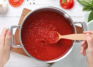 Ruční míchání italské rajčatové omáčky v hrnci s čerstvými ingrediencemi.