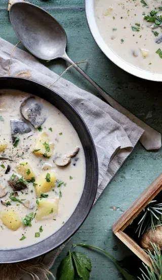 Bílá houbová polévka v tmavé misce s petrželkou.