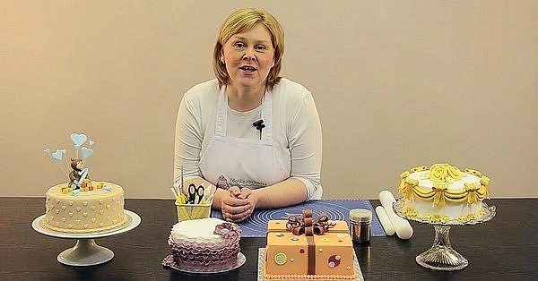 Žena s různě zdobenými dorty a náčiním na dekoraci.