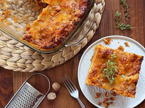 Kousek pečené lasagne s mletým masem na bílém talíři.