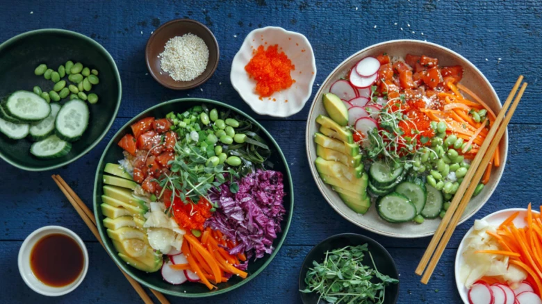 Dva poké bowl s čerstvými surovinami na tmavě modrém dřevěném povrchu.