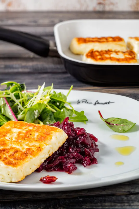Grilovaný sýr halloumi podávaný se salátom a červeným zelím na bílém talíři.