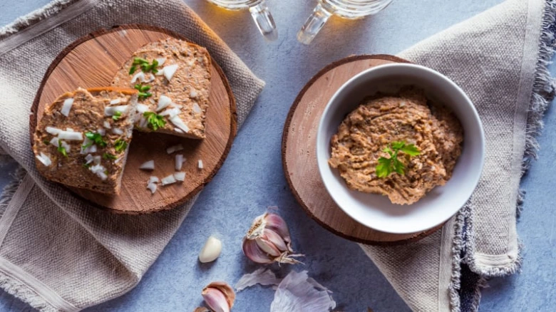 Hummus na chlebíčku s cibulí a petrželkou v bílé misce.