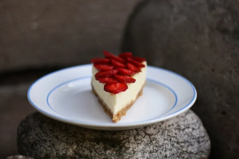 Kousek jahodového cheesecaku s čerstvými jahodami na talíři.