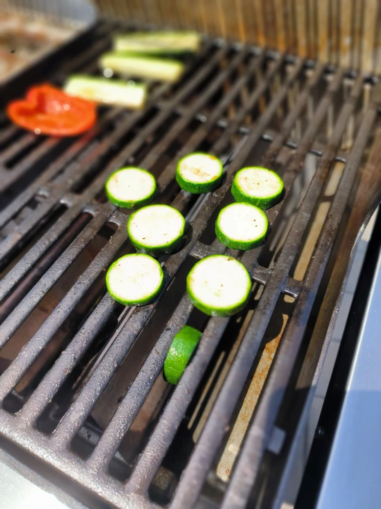 Grilované plátky cukety na mřížce grilu.