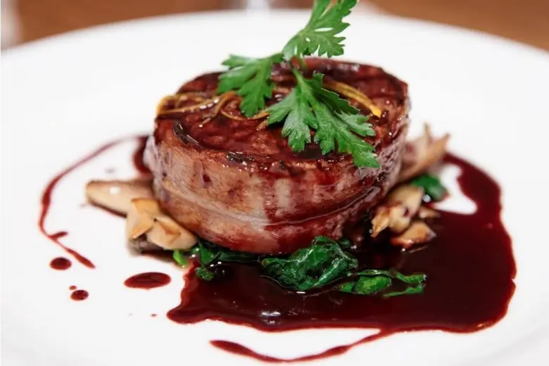Steak s omáčkou, zeleninou a bylinkami na bílém talíři.
