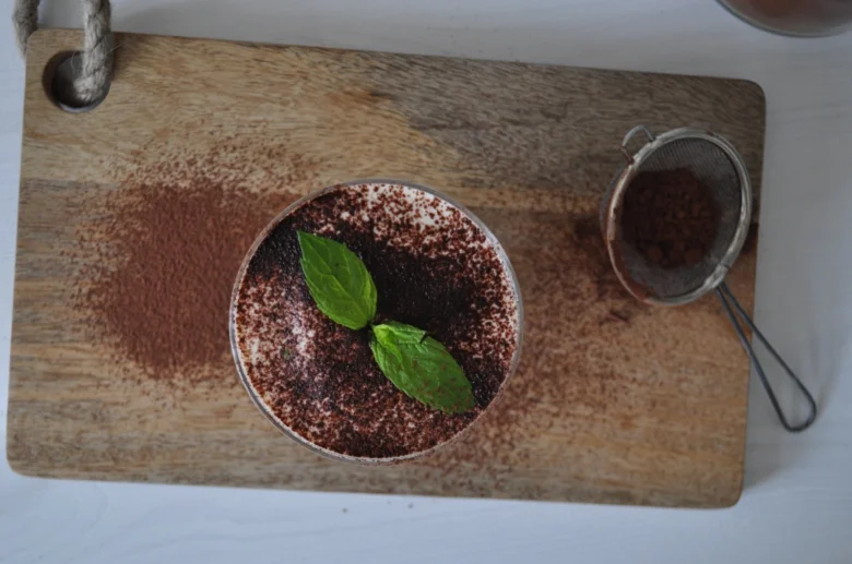 Hotový italský tiramisu s kakaem a mátou na dřevěné desce.