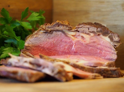 Krájené hovězí roastbeef s čerstvou petrželkou na dřevěném talíři.