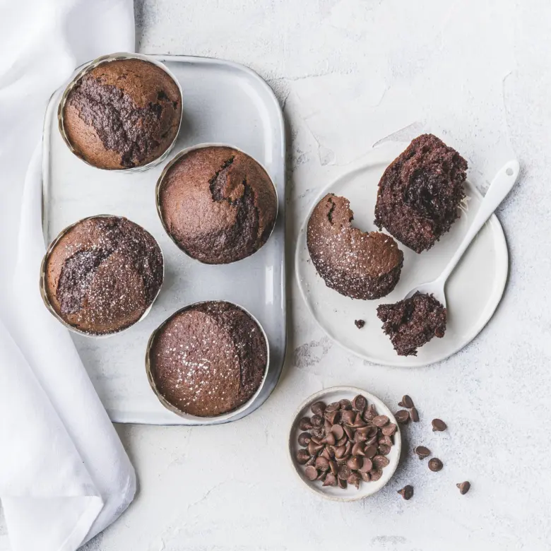 Čokoládové muffiny v plechových formách po pečení s rozbitým kouskem.