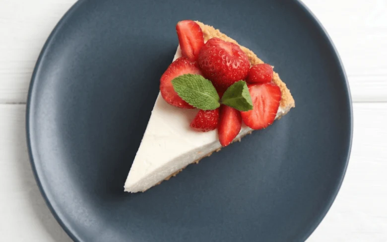 Kousek jahodového cheesecaku s čerstvými jahodami na tmavé talíři.