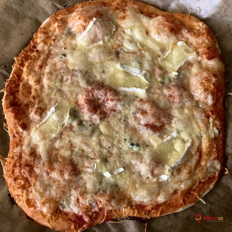 Domácí pizza s rozteklým sýrem a bylinkami na pečicím papíru.