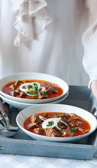 Goulash with meat and onions in bowls on tray