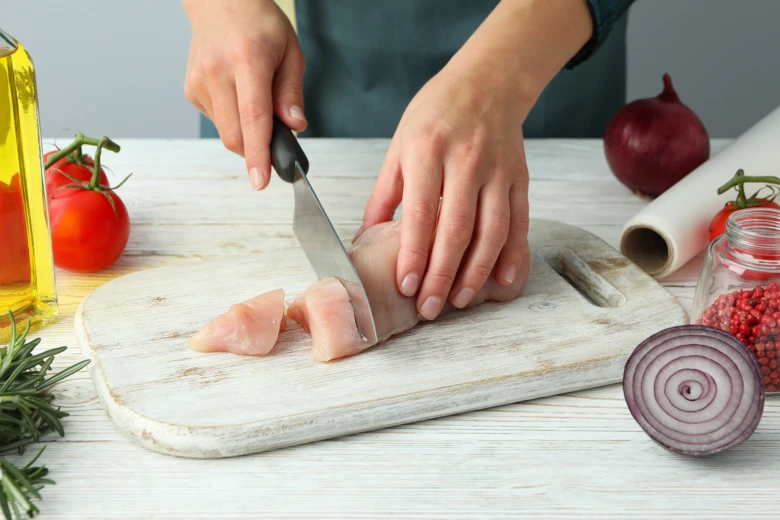Rezařka řezá kuře na proužky s čerstvými ingrediencemi.