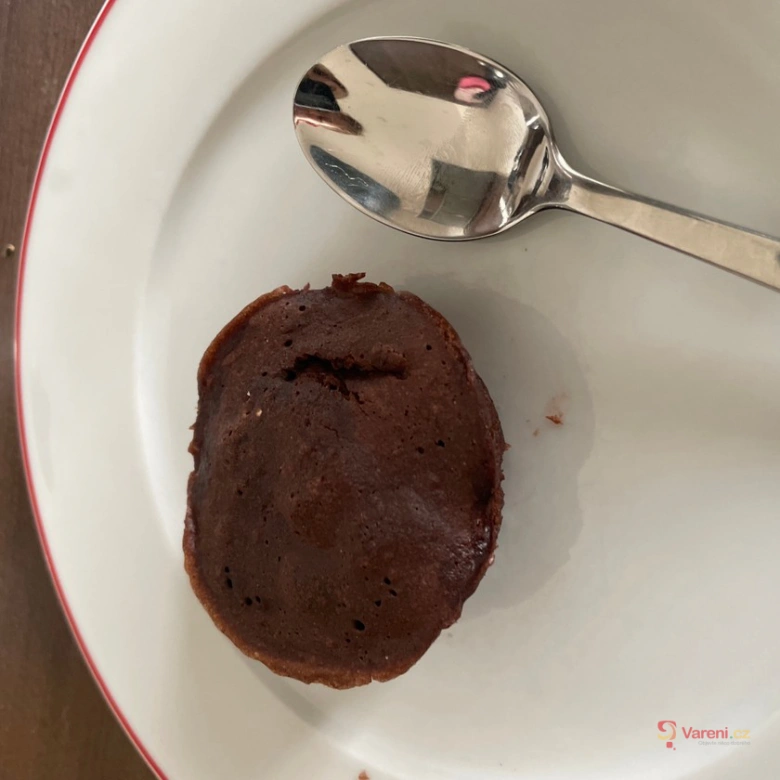 Hot čokoládový mugcake na bílém talíři s lžící vedle.