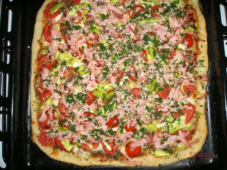 Připravená nekynutá pizzová báse s uzeným masem na plechu.