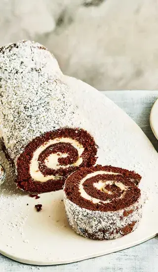 Kousk kakaové rolády s krémem posypaný cukrem.