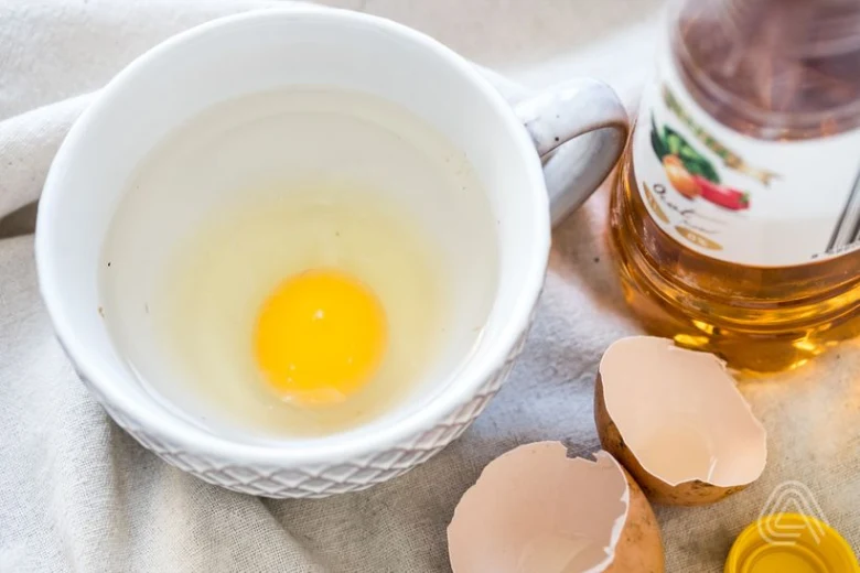 Surové vejce v šálku s olejem a skořápky pro recept na ztracená vejce.
