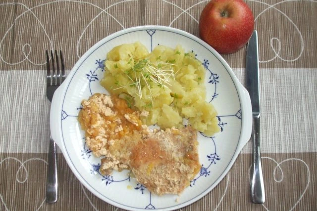 Připravené vepřové kotlety s bramborami a jablkem na talíři.