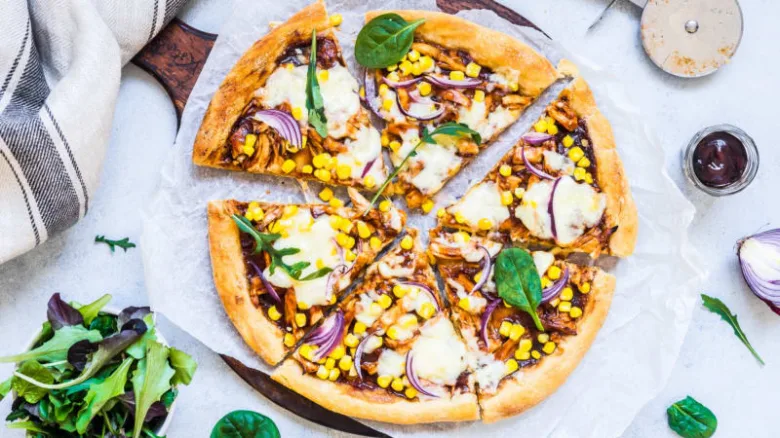 Domácí pizza na plechu s kukuřicí, cibulí a bazalkou.