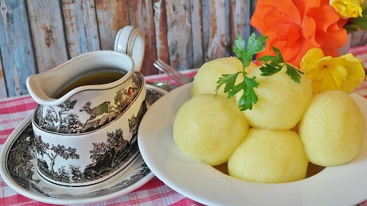 Kynuté knedlíky s omáčkou na talíři vedle lžíce.