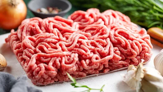 Surové mleté hovězí maso na bílém prkénku s kořením