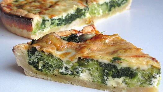 Kousek brokolice sýrové quiche na bílém podkladu.