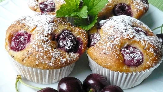 Tři třešňové muffiny posypané cukrem s čerstvou mátou.