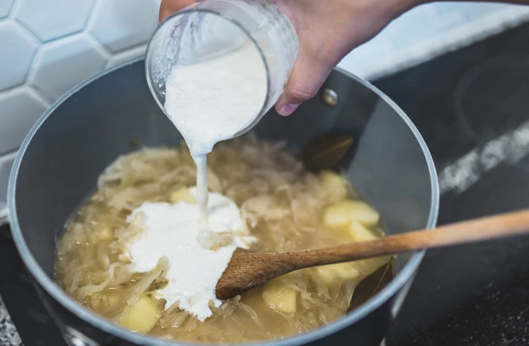 Přidávání smetany do vařené zelňačky s bramborami.