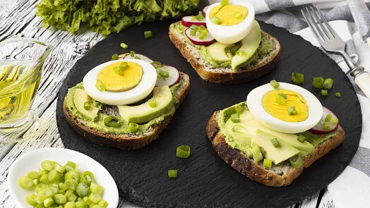 Tři toasty s avokádem, vejcem a ředkvičkami na černém podnosu.