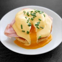 Jajka benedict s holandskou omáčkou a cibulkou na talíři.