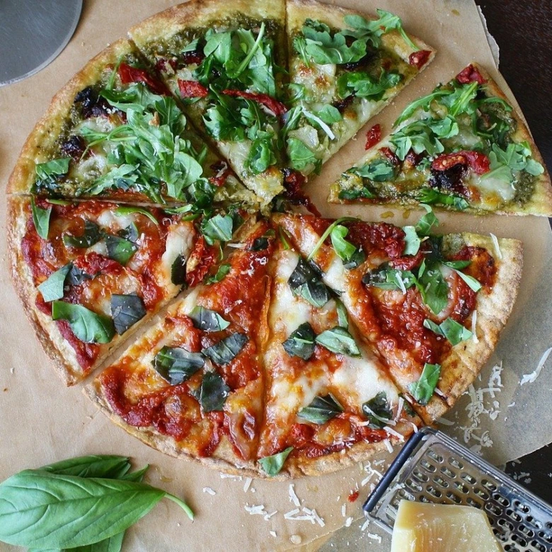 Připravená nekynutá pizza s bazalkou, rukolou a pestem na pečicím papíru.