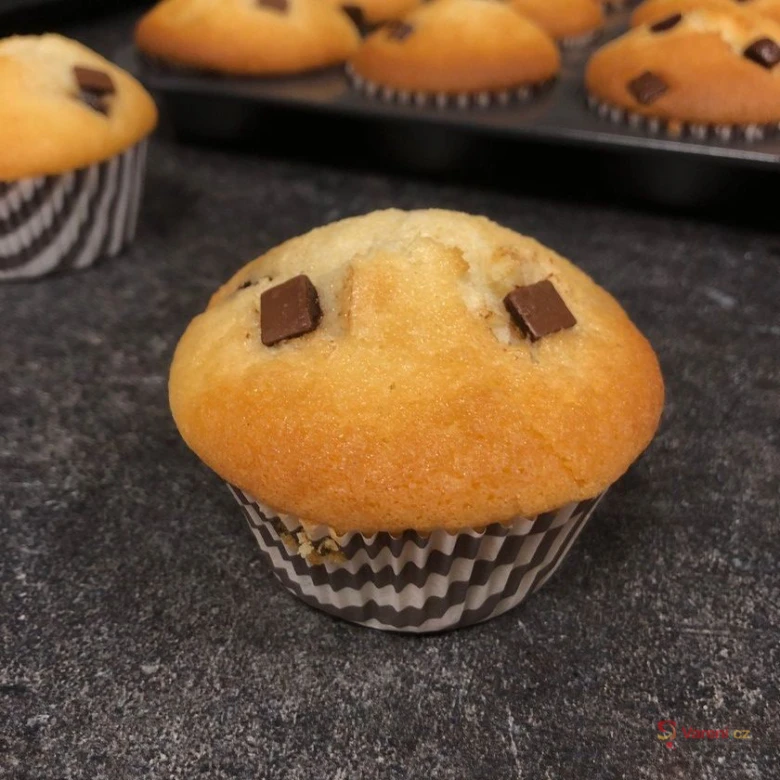 Svěžě upečený muffin s čokoládovými kousky na tmavé desce.