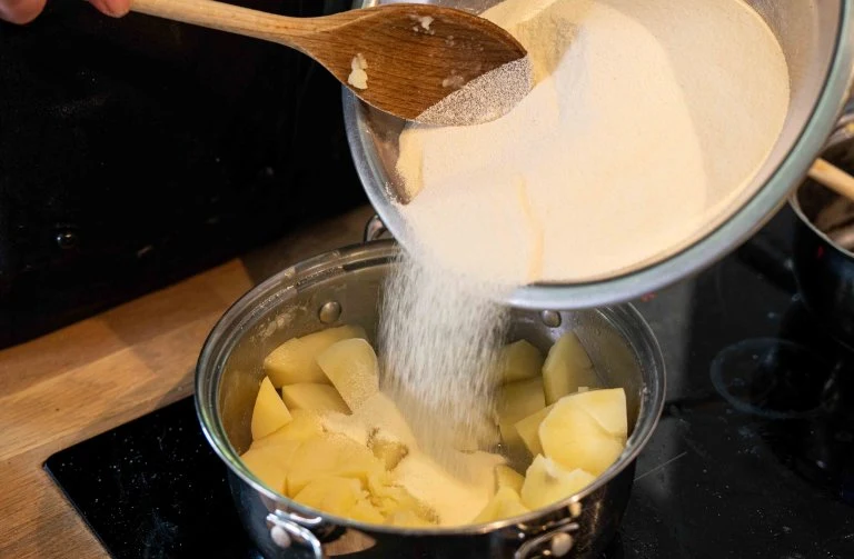 Přelévání mouky na nakrájené brambory do hrnce.