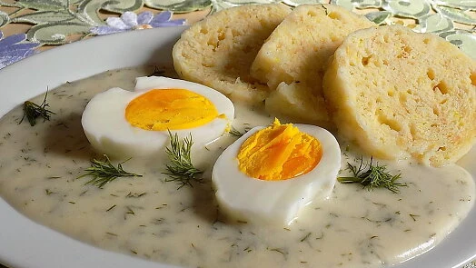 Koprová omáčka s vejcem a bramborovými knedlíky na talíři.