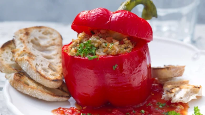 Plněná červená paprika s chlebem na bílém talíři.